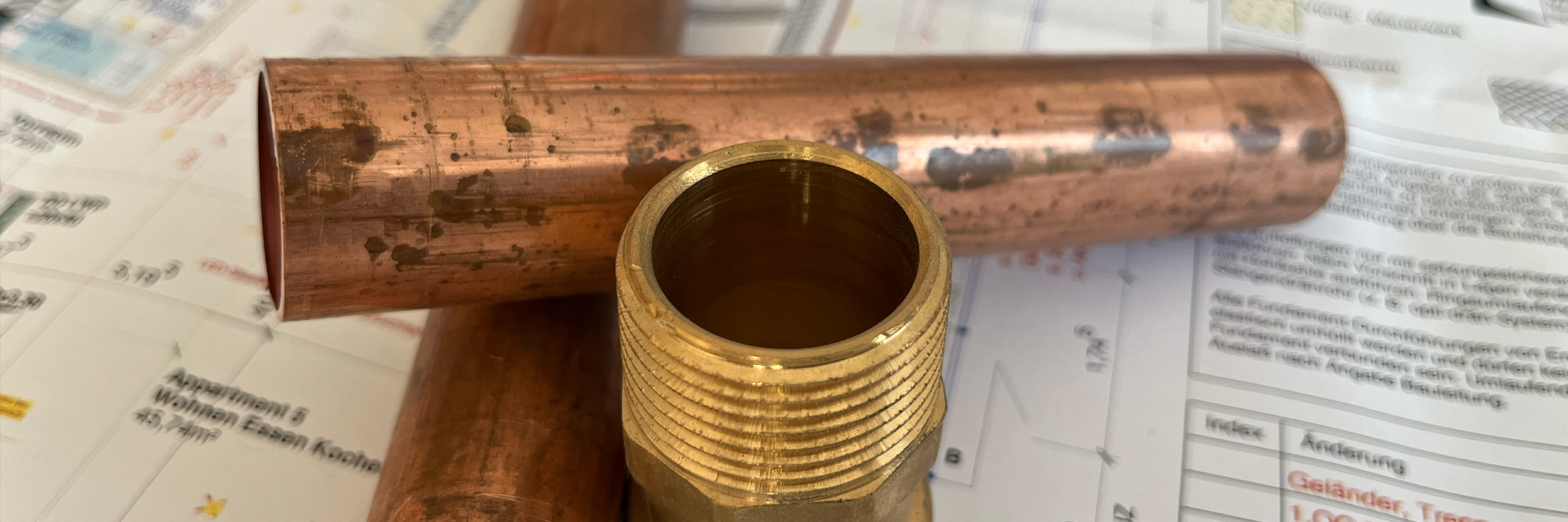 Kupferrohre und Messingfitting liegen auf Bauplan.